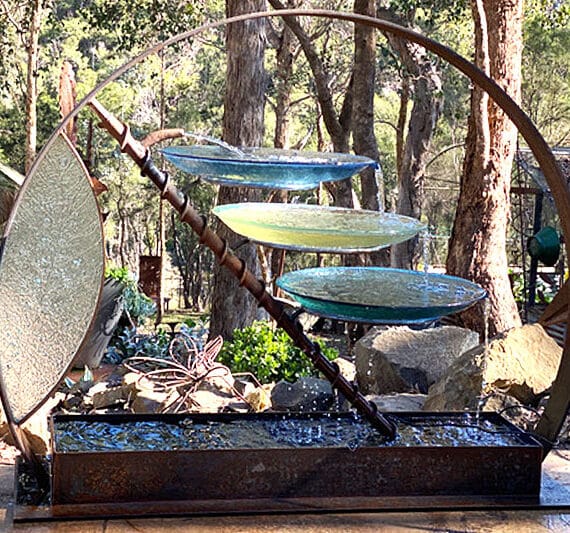 Birdbath made of reclaimed and new rolled steel, with handcrafted glass bowls and a glazed side panel that catches the light.